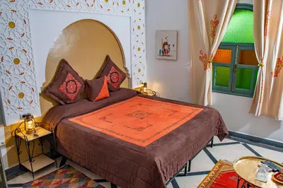 a bedroom with a large bed with an orange blanket at Le Petit Riad Maison d'hôtes in Ouarzazate