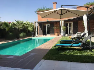 a pool with two lounge chairs and an umbrella at Villa Cactus in Ben Larbi