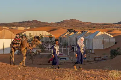 two men standing next to a camel in the desert at Milky Way Desert Camp in Merzouga