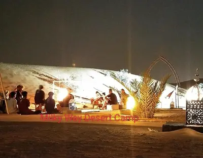 a group of people sitting on a beach at night at Milky Way Desert Camp in Merzouga