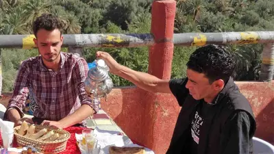 two men sitting at a table with a bottle on top at Kasbah Omari in Tinerhir