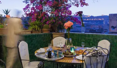 a table and chairs on a balcony with flowers at Riad La Maison Verte in Fès