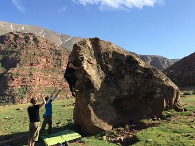 two people are climbing on a large rock at Chalet tizrag in Oukkainrdem
