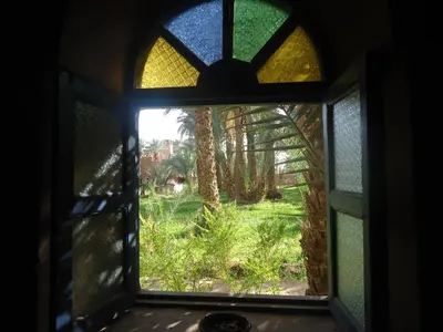 a window with a view of a garden seen through it at Riad Tagmadarte Ferme d'Hôte in Zagora