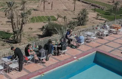 a group of people sitting at tables next to a pool at Hotel Kasbah Ennakhile - Authentic Stay in Nkob in Nkob