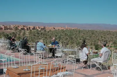 a group of people sitting at tables in front of a vineyard at Hotel Kasbah Ennakhile - Authentic Stay in Nkob in Nkob