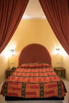 a bedroom with a bed with a red headboard and curtains at Hôtel Rif in Meknès