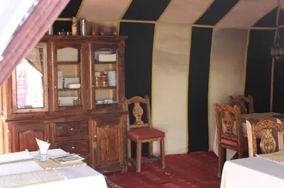 a dining room with a wooden cabinet and a chair at Asama Luxury Camp in Merzouga