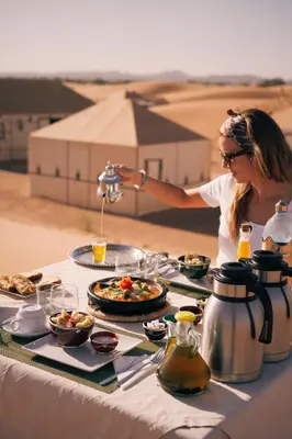 a woman is serving food at a table in the desert at Asama Luxury Camp in Merzouga