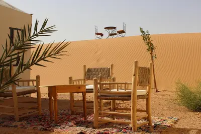 a table and chairs in front of a sand dune at Asama Luxury Camp in Merzouga