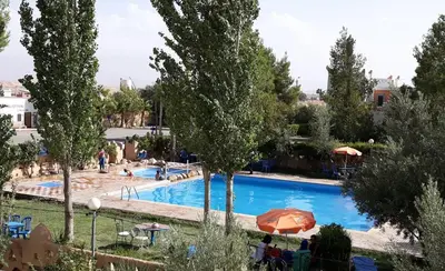 a large swimming pool with an orange umbrella and trees at Ksar Timnay Hotel in Aguelmous