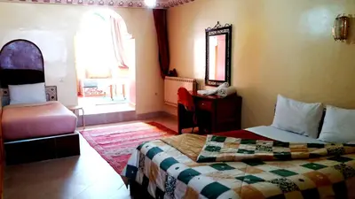 a bedroom with a bed and a desk and a window at Ksar Timnay Hotel in Aguelmous