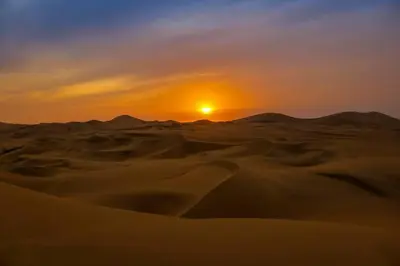 a sunset in the desert with the sun in the horizon at Karim Sahara in Zagora