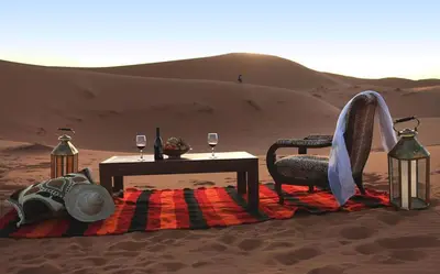 a table and chair in the desert with wine glasses at Karim Sahara in Zagora