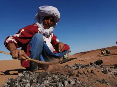 a man sitting on a pile of rocks in the desert at Maison d'hôtes Dar Farhana in Ouarzazate
