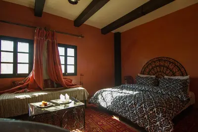 a bedroom with orange walls and two beds and a table at Rose Noire in Ouarzazate