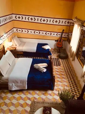a room with two beds and a guitar in it at Hôtel panoramique de la vallée in Aït Idaïr