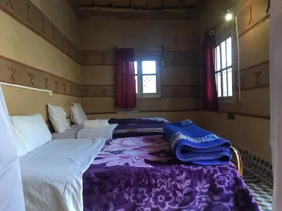 a bedroom with two beds with purple sheets and windows at Hôtel panoramique de la vallée in Aït Idaïr