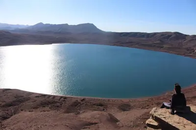 a person sitting on a rock in front of a lake at Auberge des lacs in Imilchil