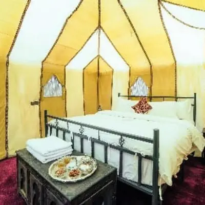 a bed in a tent with a plate of food on a table at Les Pyramides Luxury desert Camp in Merzouga