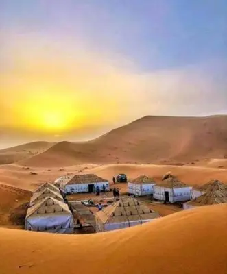a group of tents in the desert with the sunset at Les Pyramides Luxury desert Camp in Merzouga