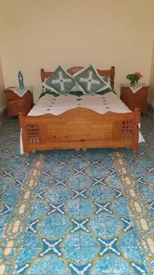 a bedroom with a wooden bed on a blue rug at Écologie oasis tafilalt CHEZ L' HABITANT in Er Rachidia