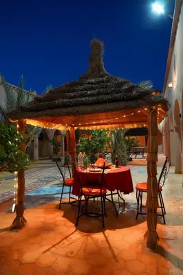 a table and chairs under a gazebo at night at Auberge Les Roches in Merzouga