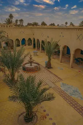 a building with a courtyard with a fountain and palm trees at Auberge Les Roches in Merzouga