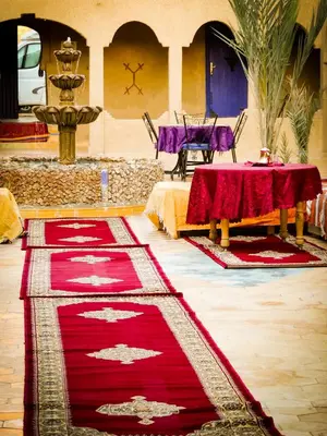a room with red carpets and a table and chairs at Auberge Les Roches in Merzouga