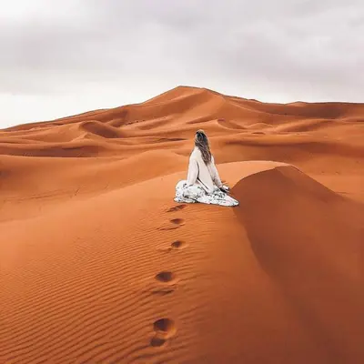 a woman sitting on a sand dune in the desert at Magic Luxury Camp in Merzouga