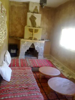 a living room with a fireplace with two tables and a rug at Complexe Collier D' Ambre in Imilchil