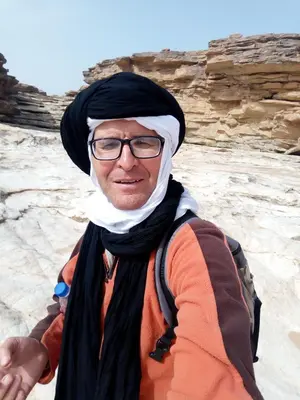 a man wearing a hijab and glasses standing in the desert at Complexe Collier D' Ambre in Imilchil