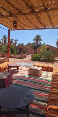 acovered patio with a table and benches and a rug at Kasbah Desert Camp in Mhamid