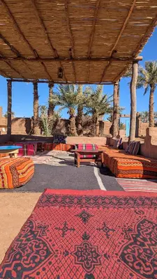 a patio with colorful rugs and tables and palm trees at Kasbah Desert Camp in Mhamid