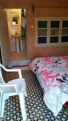 a bedroom with a bed and a chair and a sink at gîte les jardins in Goulmima