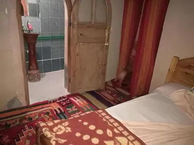 a bedroom with a bed and a door and a rug at Riad Berbère Boutaghrar in Bou Tharar