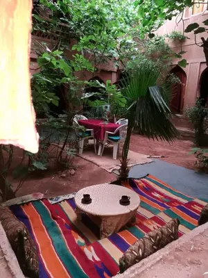 a patio with a table and a rug with a table and a tree at Riad Berbère Boutaghrar in Bou Tharar