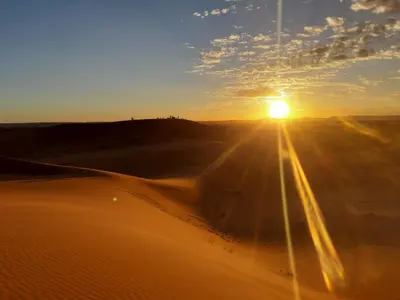 a sunset in the desert with the sun rising over the sand at Appartement belkacem in Merzouga