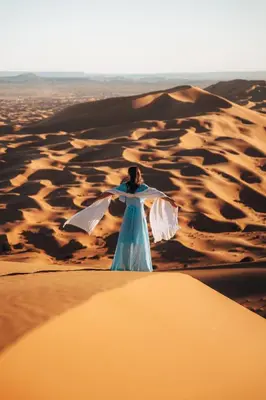 a woman in a blue dress standing in the desert at Royal Luxury Camp in Merzouga
