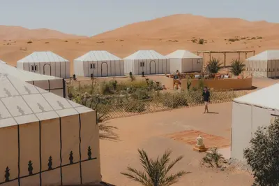 a person walking in the desert with buildings and a desertermott at Royal Luxury Camp in Merzouga