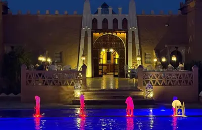 a building with pink flamingos in the water at night at Sbai Palace in Mhamid