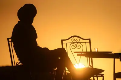 a person sitting in a chair in front of a sunset at Sahara Desert Experience camp in Merzouga