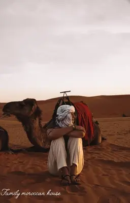 a man sitting next to a camel in the desert at Sahara Desert Experience camp in Merzouga