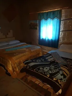 a bedroom with two beds and a window with a curtain at Family Moroccan House in Merzouga