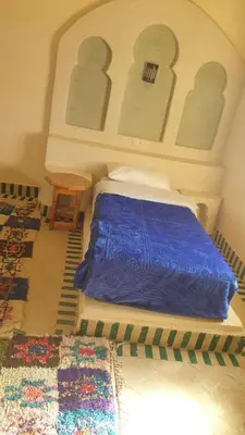 a bedroom with a bed with a blue blanket and a table at Kasbah Tamariste in Merzouga