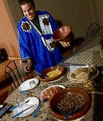 a man in apron standing at a table with food at Kasbah Tamariste in Merzouga
