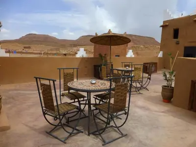 a patio with tables and chairs and an umbrella at Kasbah La Cigogne in Aït Ben Haddou