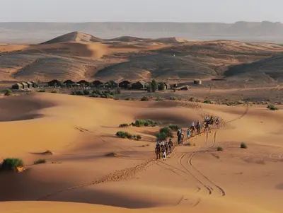 a group of people riding horses through the desert at Tassili Luxury Desert Camp in Merzouga