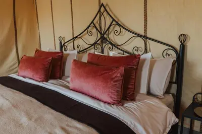 a bed with three red pillows on it at Tassili Luxury Desert Camp in Merzouga