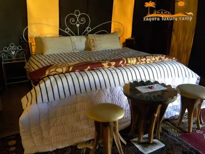 a bedroom with a bed with stools next to a table at Sahara Luxury Camp in Zagora